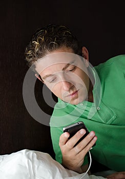 Handsome young man looking at cell phone at night in bed