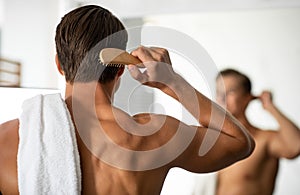 Handsome young man looking in the mirror brushing his hair