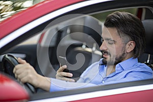 Handsome young man looking at the phone while driving