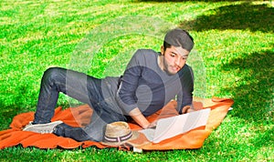 Handsome young man looks surprised in the park sitting on the grass with a laptop
