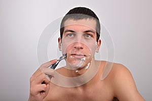 Handsome young man with lots of shaving cream on his face preparing to shave with razor
