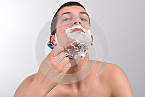 Handsome young man with lots of shaving cream on his face preparing to shave with razor