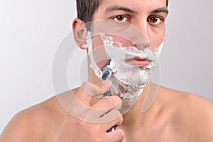 Handsome young man with lots of shaving cream on his face is sha