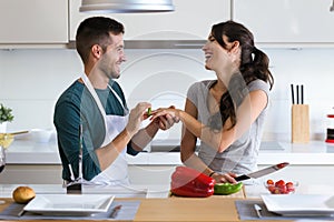 Handsome young man making the joke of asking his girlfriend to marry with a bell pepper in the kitchen at home.