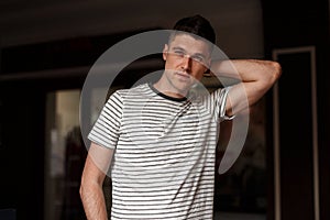 Handsome young man model with stylish hairstyle with beautiful gray eyes in a fashionable striped t-shirt posing standing