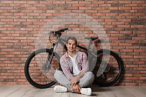 Handsome young man with modern bicycle near brick wall