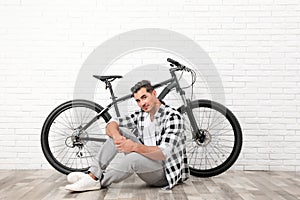 Handsome young man with  bicycle near white brick wall indoors