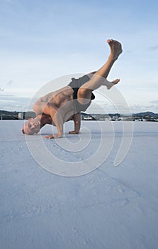 Handsome young man with naked torso doing brake dancing movements on a rooftop