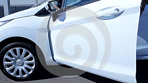 Handsome young man opening car front door getting out of white modern brand new automobile vehicle