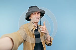 Handsome young man in panama and shirt shows thumbs up with a smile on his face and looks at the camera with a smile on his face