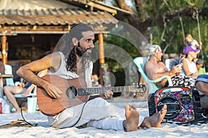 Handsome young man playing guitar on the beach during sunset at tropical island Koh Phangan, Thailand