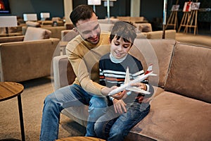 Handsome young man playing toys plane with his younger brother while resting in the VIP lounge in the airport departure terminal