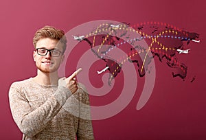 Handsome young man pointing at world flight map on color background