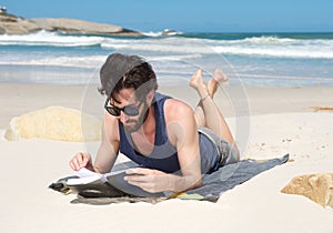 Handsome young man reading book at the beach