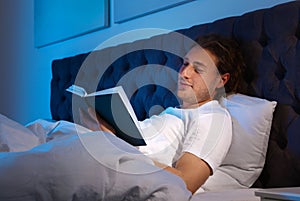 Handsome young man reading book in dark room at night