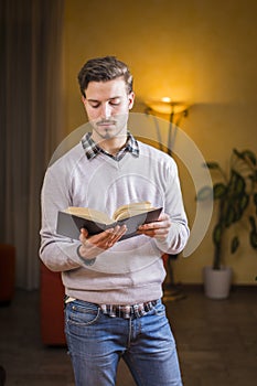 Handsome young man reading book at home in his living-room