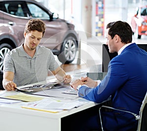 Handsome young man reading a booklet at the dealership showroom.