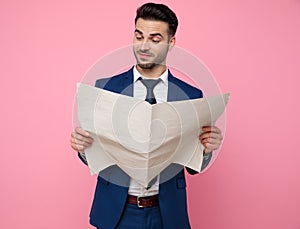 Handsome young man reading newspaper on pink background