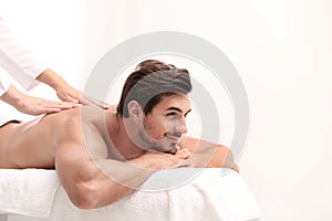 Handsome young man receiving back massage on light background. Spa salon