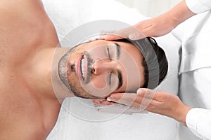 Handsome young man receiving face massage on spa table