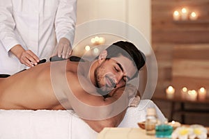 Handsome young man receiving hot stone  in spa salon, space for text