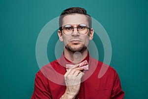 Handsome young man in a red shirt correcting bow-tie against a green background photo