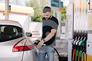 Handsome young man refueling car at gas station. Male filling diesel at gasoline fuel in car using a fuel nozzle.