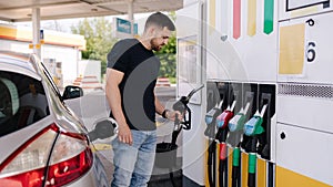 Handsome young man refueling car at gas station. Petrol concept. Side view