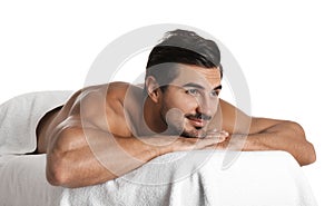 Handsome young man relaxing on massage table against white background