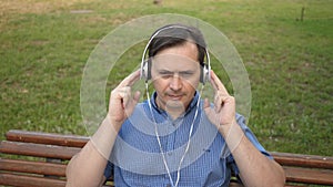 Handsome young man resting in a park listening to music from his smartphone with headphones and dancing outside in a