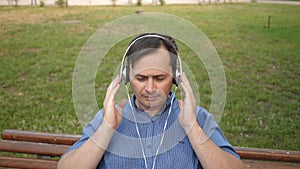 Handsome young man resting in a park listening to music from his smartphone with headphones and dancing outside in a