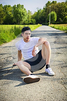 Handsome young man resting sitting on road after