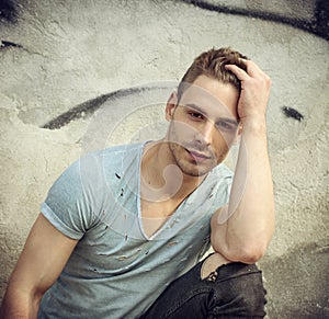 Handsome young man with ripped jeans sitting outdoor