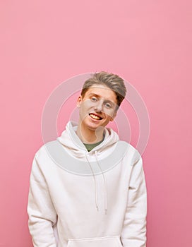 Handsome young man in roe deer stands on a pink background, looks into the camera and smiles, wearing a white hoodie. Positive