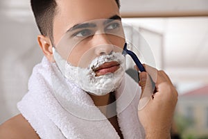 Handsome young man shaving with razor in bathroom, closeup