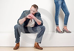 Handsome young man sitting alone with female legs standing