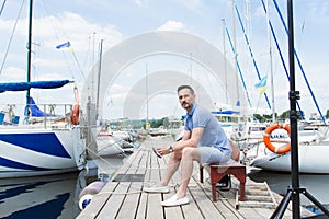 Handsome young man sitting on bench in dock of the bay between boats. man on pier looking away.