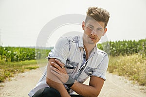 Handsome young man sitting in coutryside dirt road