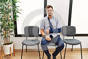 Handsome young man sitting at doctor waiting room with arm injury looking sleepy and tired, exhausted for fatigue and hangover,