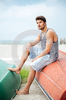 Handsome young man sitting on a fishing boat by sea