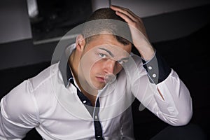 Handsome young man sitting on the floor, hand on his head