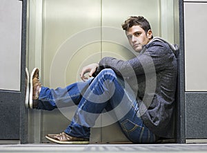 Handsome young man sitting in front of elevator doors