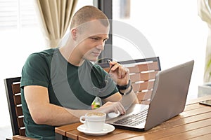Handsome young man sitting, holding glasses and looking in laptop