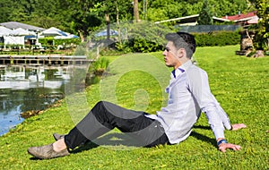 Handsome young man sitting on lawn nexto to a lake