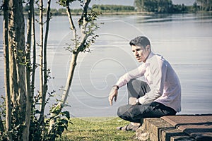 Handsome young man sitting on lawn nexto to a lake