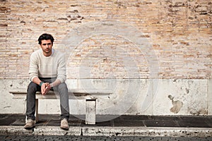 Handsome young man sitting on marble bench with bricks background