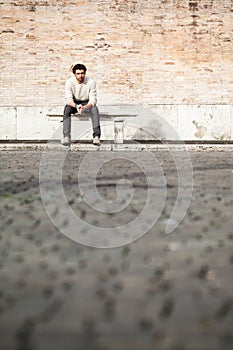 Handsome young man sitting on marble bench with bricks background