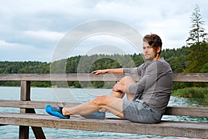 Handsome young man sitting near lake at sunny day. Recreation in nature concept
