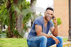 Handsome young man sitting on sidewalk and talking on mobile phone