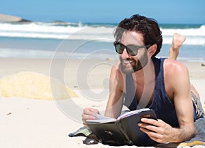 Handsome young man smiling and reading book on the beach